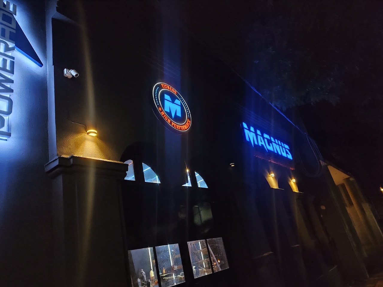 Frente del gimnasio Magnus Fitness de noche con cartel de neón azul iluminado